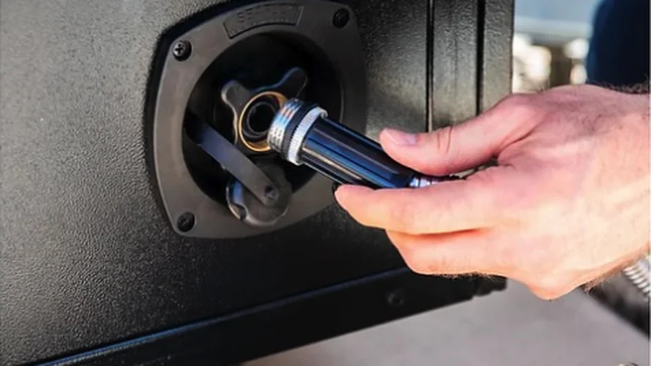 A hand threading a garden hose fitting into the round water inlet on the side of the Banger's cabinet.