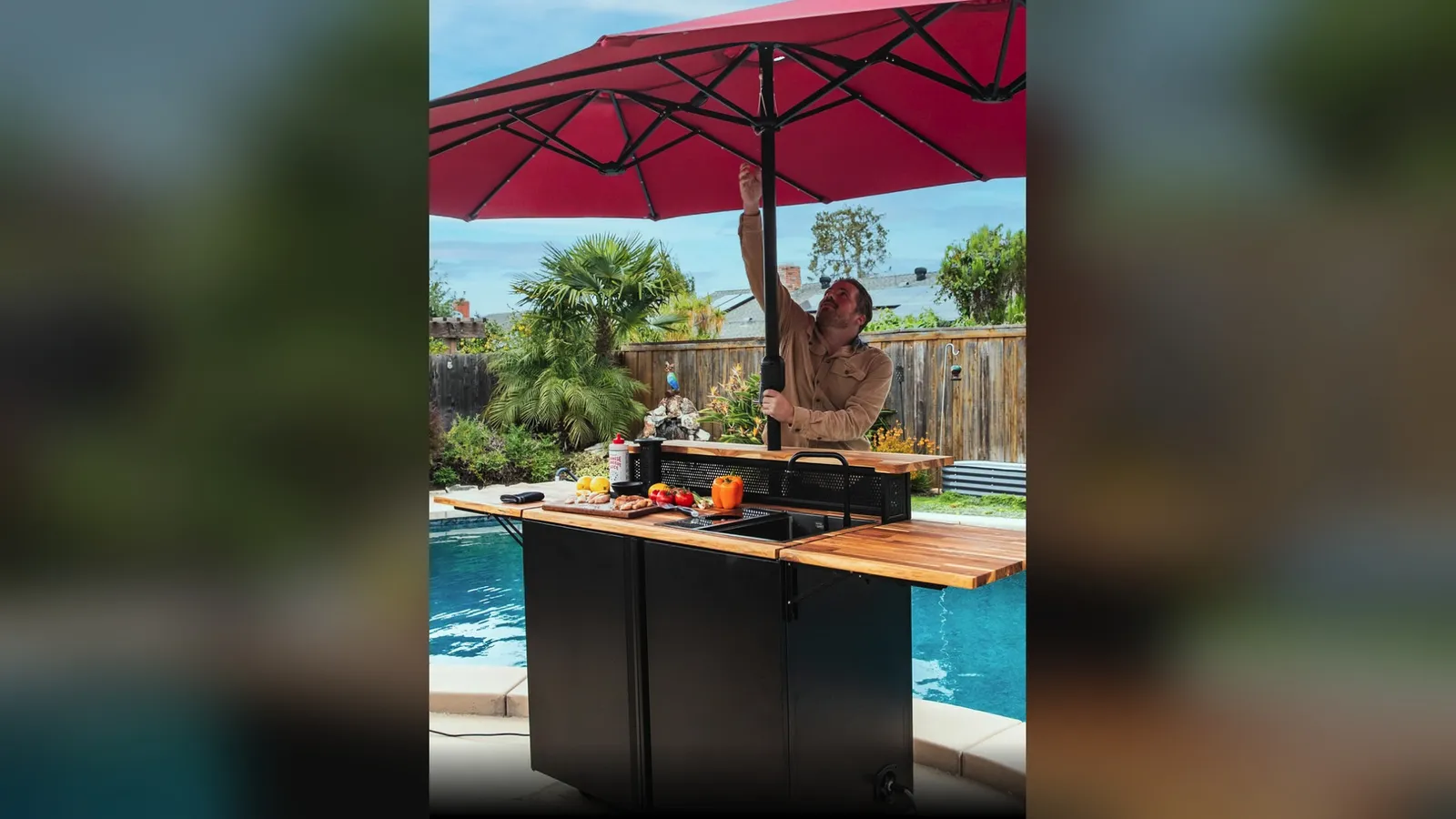 A man raising a red patio umbrella through the Banger's center pole beside a pool.